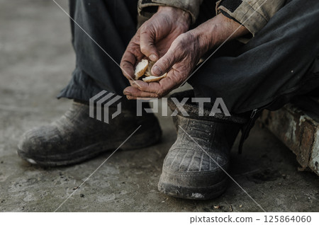 The tired hands clutch the crumbs as if they were precious. The hands are cracked from years of labor. 125864060