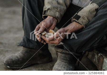 The trembling hands carefully hold the last bits of bread. The hands are dirty, marked by time and struggle.  125864061