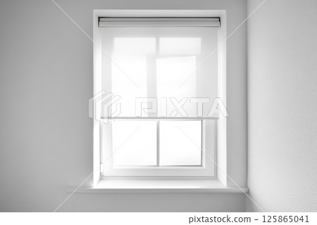 Minimalist interior with a closed white roller blind on a modern window. Soft daylight filters through the translucent fabric, creating a clean, serene and bright atmosphere. Perfect for design themes Minimalist interior with a closed white roller blind on a modern window. Soft daylight filters through the translucent fabric, creating a clean, serene and bright atmosphere. Perfect for design themes 125865041