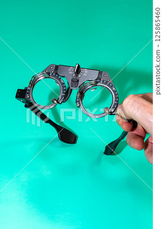 Man Hand Holding A Pair of Test Glasses on a Green Table Man Hand Holding A Pair of Test Glasses on a Green Table 125865460
