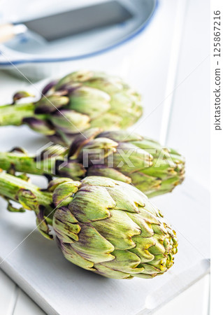 Ripe artichokes plant on white cutting board. 125867216