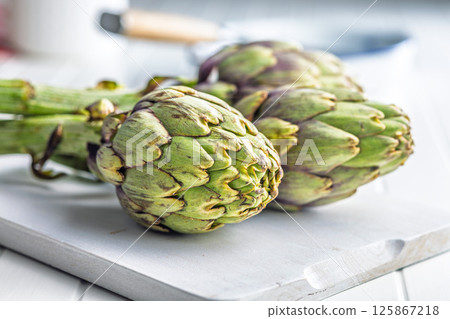 Ripe artichokes plant on white cutting board. Ripe artichokes plant on white cutting board. 125867218