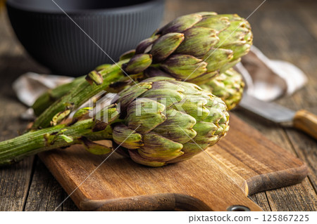 Ripe artichokes plant on cutting board on wooden table. 125867225