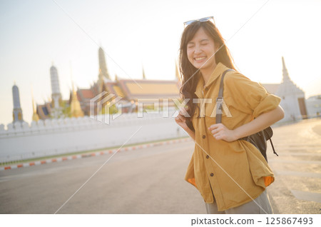 Southeast asian woman travel concept happy smiling with backpack near temple in warm sunlight Southeast asian woman travel concept happy smiling with backpack near temple in warm sunlight 125867493