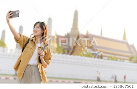 Southeast asian woman travel concept is captured as she joyfully takes selfie in front of historic temple, showcasing her excitement and cultural beauty of destination Southeast asian woman travel concept is captured as she joyfully takes selfie in front of historic temple, showcasing her excitement and cultural beauty of destination 125867501
