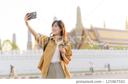 Southeast asian woman takes travel selfie with joyful expression in front of historic temple, capturing vibrant concept of exploration and cultural adventure 125867502