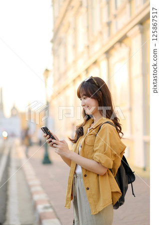 Southeast asian woman enjoys travel concept using her phone outdoors in warm light setting showing relaxed and happy mood Southeast asian woman enjoys travel concept using her phone outdoors in warm light setting showing relaxed and happy mood 125867517