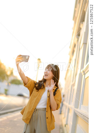 Southeast asian woman travel concept selfie happy young female taking photo outdoors in city street during sunset light 125867522