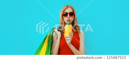 Fashion portrait of beautiful young woman with colorful shopping bags drinking juice in red dress 125867523