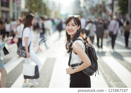 Southeast asian woman smiling with backpack walking on busy city street crosswalk in daylight Southeast asian woman smiling with backpack walking on busy city street crosswalk in daylight 125867587