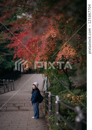 Southeast asian woman enjoys travel concept standing on stone pathway under colorful autumn leaves with peaceful expression in natural outdoor setting 125867704