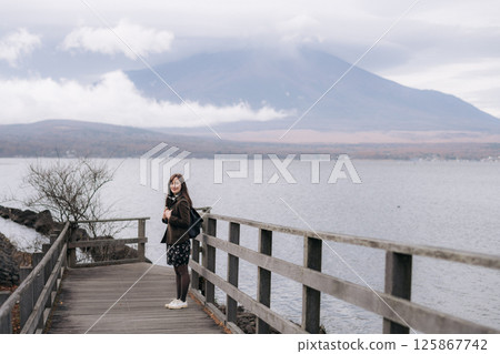 Southeast asian woman enjoys travel concept by standing on wooden bridge near calm lake with mountain covered in clouds in background creating peaceful atmosphere Southeast asian woman enjoys travel concept by standing on wooden bridge near calm lake with mountain covered in clouds in background creating peaceful atmosphere 125867742