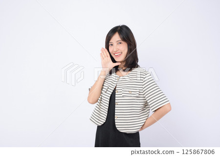 Southeast asian woman smiling and advertising with hand gesture wearing striped jacket and black dress on white background Southeast asian woman smiling and advertising with hand gesture wearing striped jacket and black dress on white background 125867806