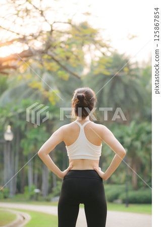 Southeast asian woman stands in park representing wellness and healthy lifestyle concept as she prepares for exercise in morning surrounded by lush green nature Southeast asian woman stands in park representing wellness and healthy lifestyle concept as she prepares for exercise in morning surrounded by lush green nature 125867854