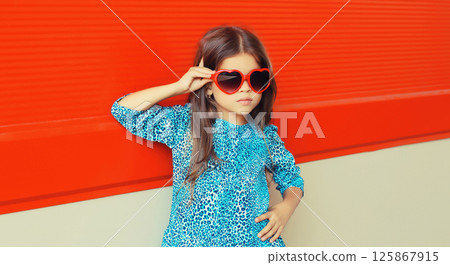 Beautiful little girl child in red heart shaped sunglasses and blue dress on city street Beautiful little girl child in red heart shaped sunglasses and blue dress on city street 125867915