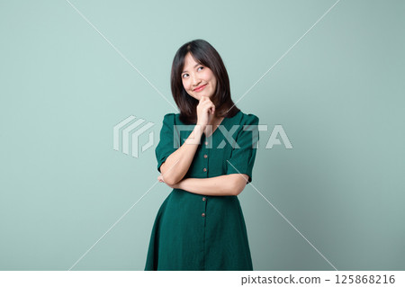 Southeast asian woman in green dress poses thoughtfully with smile, perfect for advertising concepts and creative marketing ideas 125868216