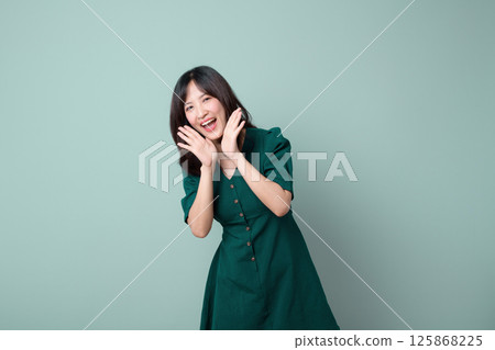 Happy southeast asian woman in green dress poses joyfully for advertising with bright smile and playful hands near her face Happy southeast asian woman in green dress poses joyfully for advertising with bright smile and playful hands near her face 125868225