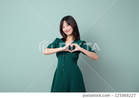 Southeast asian woman in green dress is smiling warmly while making heart shape with her hands for advertising love and kindness Southeast asian woman in green dress is smiling warmly while making heart shape with her hands for advertising love and kindness 125868227