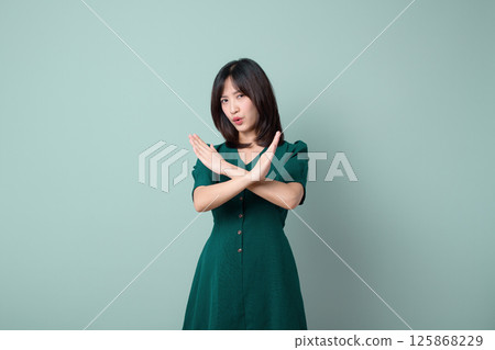 Southeast asian woman in green dress shows stop gesture with crossed arms expressing refusal for advertising or promotion in plain background 125868229