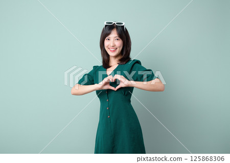 Southeast Asian woman in green dress making heart shape with hands smiling for advertising campaign with positive and friendly expression 125868306