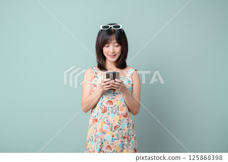Southeast asian woman is happily using mobile phone to access internet application while standing against plain background Southeast asian woman is happily using mobile phone to access internet application while standing against plain background 125868398