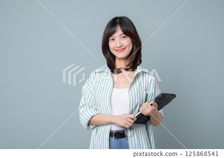 Southeast asian woman smiling gently while holding tablet device showing confidence and ease in online shopping and digital interaction in casual setting 125868541