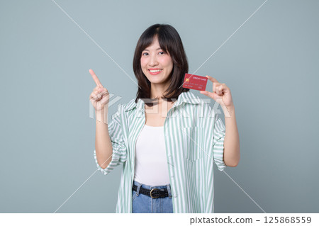 Southeast asian woman shopping online with credit card smiling and pointing up on gray background showing happiness and confidence 125868559