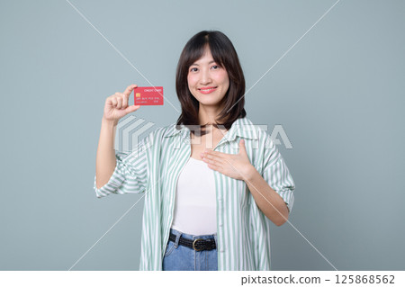 Southeast asian woman is happily shopping online holding credit card and smiling confidently while standing against plain background in casual clothes 125868562