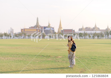 Southeast asian woman enjoys travel concept by exploring vast green field near historic temple complex, smiling happily as she embraces cultural adventure outdoors Southeast asian woman enjoys travel concept by exploring vast green field near historic temple complex, smiling happily as she embraces cultural adventure outdoors 125868604