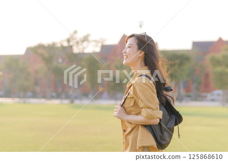 Southeast asian woman travel concept smiling outdoors with backpack in park during sunset Southeast asian woman travel concept smiling outdoors with backpack in park during sunset 125868610