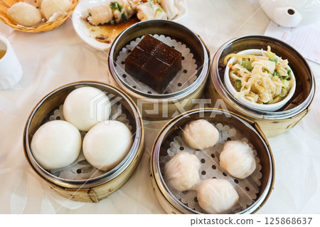 close up of Cantonese Hong Kong style yum cha dim sum in bamboo steamer including red date cake, shrimp dumplings, ginger beef tripe and white Creamy Custard Bun close up of Cantonese Hong Kong style yum cha dim sum in bamboo steamer including red date cake, shrimp dumplings, ginger beef tripe and white Creamy Custard Bun 125868637