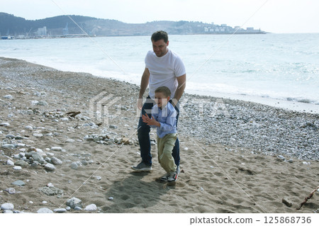 young father playing with his son with rock on beach, happy lifestyle family young father playing with his son with rock on beach, happy lifestyle family 125868736