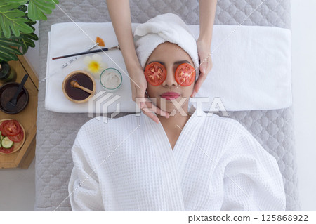 Relaxed young asian woman getting eye nature treatment by tomato at spa salon. Wellness and healing concept. Relaxed young asian woman getting eye nature treatment by tomato at spa salon. Wellness and healing concept. 125868922