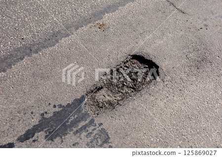 A significant pothole disrupts the smooth surface of a city street, indicating wear from vehicles and weather conditions 125869027