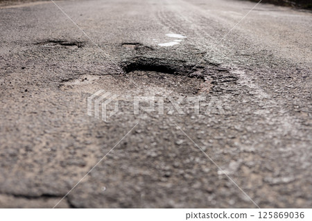 A neglected street features significant road damage with deep potholes and cracked asphalt, highlighting the need for repairs and maintenance 125869036