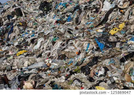 A vast pile of mixed waste is visible, showcasing discarded textiles, plastics, and debris. This landfill reflects ongoing environmental challenges 125869047