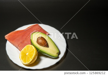 Avocado, red fish with lemon on a black background 125869212