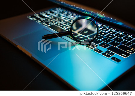 A magnifying glass is placed on a notebook computer. Search for viruses on a laptop computer A magnifying glass is placed on a notebook computer. Search for viruses on a laptop computer 125869647