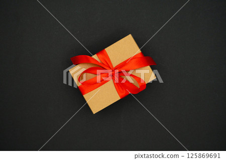 Present box from brown paper with red ribbon bow, isolated on black background. Celebration concept Present box from brown paper with red ribbon bow, isolated on black background. Celebration concept 125869691