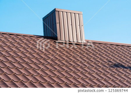 The roof of a house with modern metal tiles and a chimney, against the background of a blue sky. Metal roofing 125869744