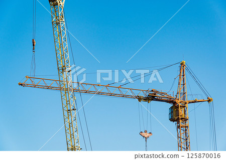 Two yellows hoisting cranes with blue sky background. Machines for construction. Construction concept 125870016