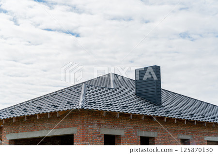 A new brick house with a black roof. Construction of a house. Roof construction 125870130