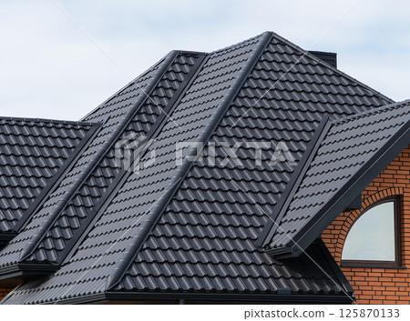 The house, the roof of which is covered with black metal tiles. Black tiles roof on a new house 125870133
