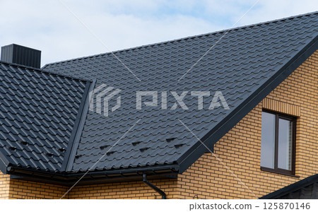 A roof made of metal tiles with a chimney against a cloudy sky 125870146