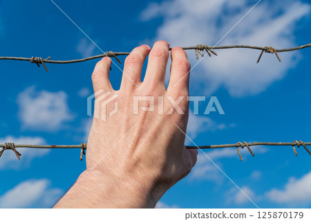 A hand holds a barbed wire against the sky. Refugee. Freedom concept 125870179