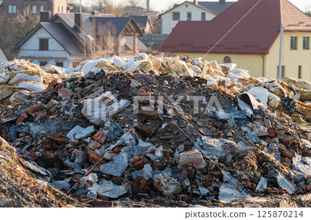 Dumping area and city building. Landfill of garbage near houses. Environmental pollution from construction waste 125870214