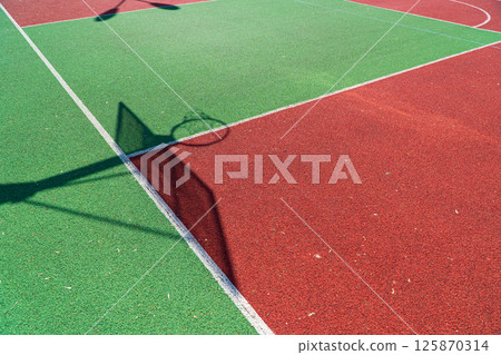 Shadow of the rack with shield and basketball ring on basketball field. Colorful basketball lines on an outdoor court 125870314