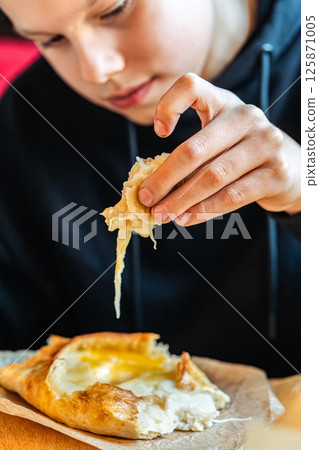 Boy tearing off cheesy bread from khachapuri with egg, close-up view, concept of traditional Georgian cuisine 125871005