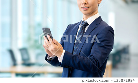 拿著智慧型手機的微笑的男性商人 拿著智慧型手機的微笑的男性商人 125871984