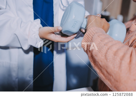Physiotherapist training with patient using dumbbells in clinic,Physical therapy concept 125872088